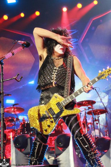 Musician in stage outfit performing with a guitar, dramatic lighting, and vibrant atmosphere.