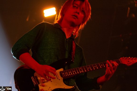 Musician playing electric guitar on stage with dramatic lighting.