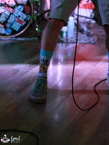 A close-up of a musician's legs wearing colorful socks and casual shoes onstage.