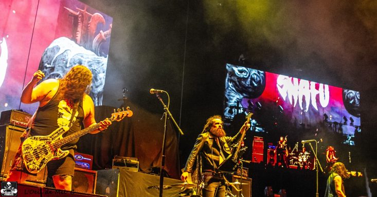 Band performing live on stage with vibrant lighting and a large screen in the background.