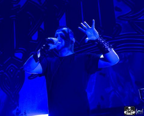 Male vocalist in a black shirt performs passionately with hands raised on stage.