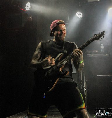 Straightline - L'Anti-Bar & Spectacles Male musician passionately playing an electric guitar on stage, wearing a cap and tank top.