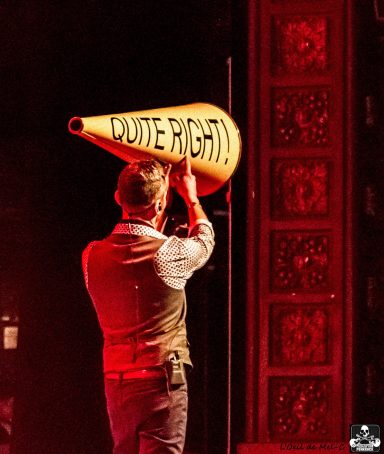 Person in a vest holding a large megaphone that reads "SHOUT RIGHT!" with dramatic lighting.