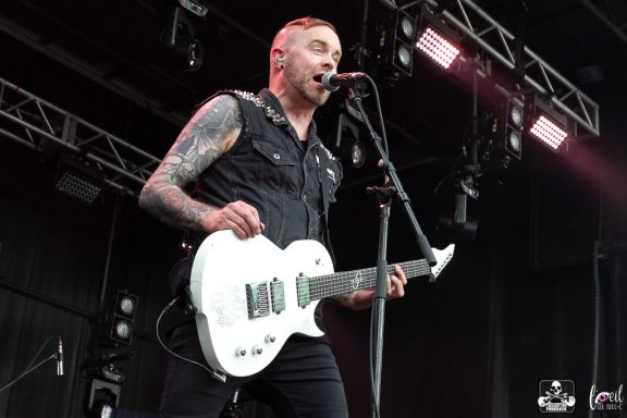 A musician singing into a microphone while playing an electric guitar on stage.