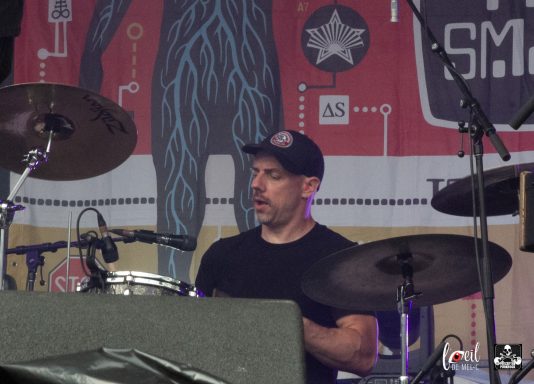 A drummer performing on stage, focused on his instrument with a vibrant backdrop.