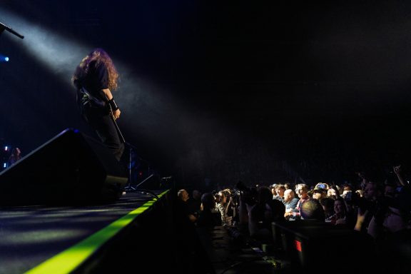 A musician performs on stage with spotlight, while an audience watches eagerly.