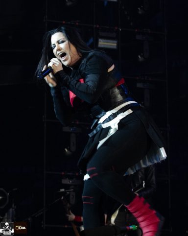 Singer performing on stage with dramatic expression, wearing a black outfit and pink accents.
