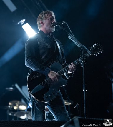 A musician singing into a microphone while playing an electric guitar on stage.