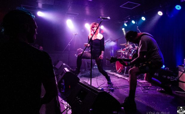 A rock band performs on stage with dramatic lighting and energetic poses.