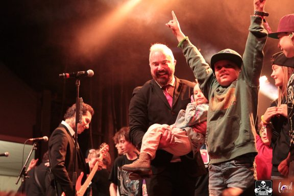 Man in a suit holds a child excitedly while performing on stage.