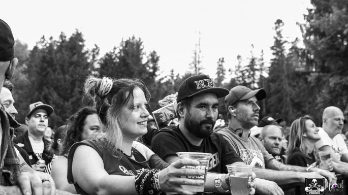 Crowd at an outdoor event, with a woman and a man holding drinks in the foreground.