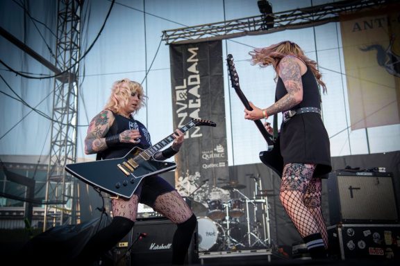 Two female musicians performing on stage, playing electric guitars with high energy.