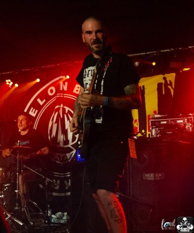 A musician playing bass guitar on stage under colorful lights.