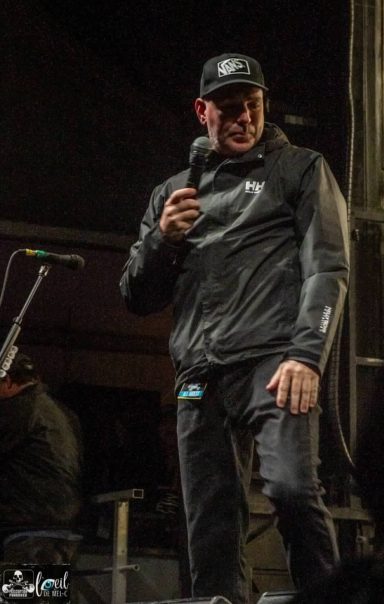 Rej Laplanche - Red Bridge Fest 2026 A performer in a black jacket and cap smiles while holding a microphone on stage.