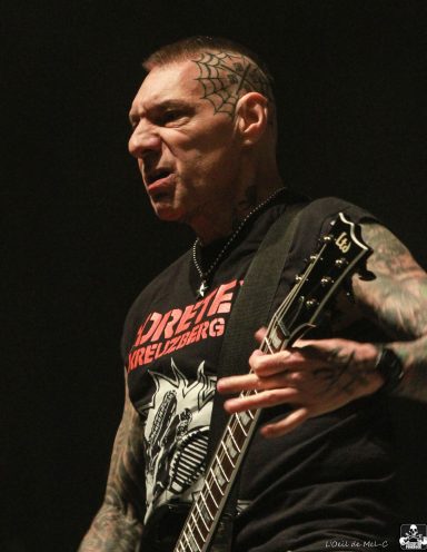 A tattooed musician passionately playing guitar on stage.