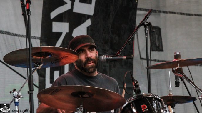 Drummer performing on stage with focused expression, surrounded by music equipment.