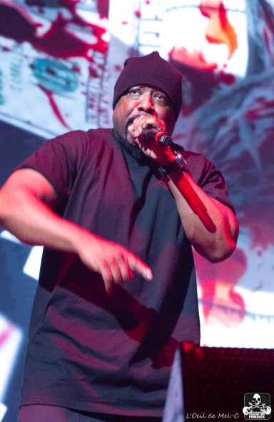 A performer in a black beanie and shirt passionately raps on stage.