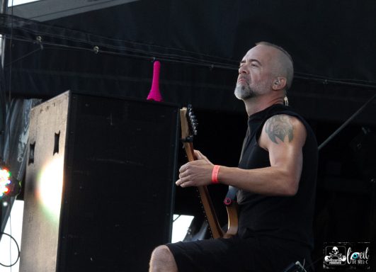 A musician playing a bass guitar on stage, wearing a sleeveless shirt.