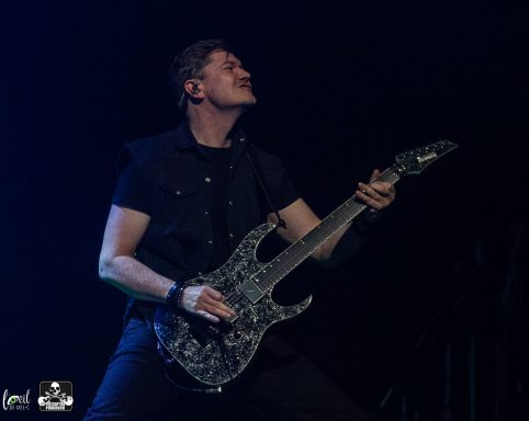 Man in black shirt playing an electric guitar on stage with intense expression.