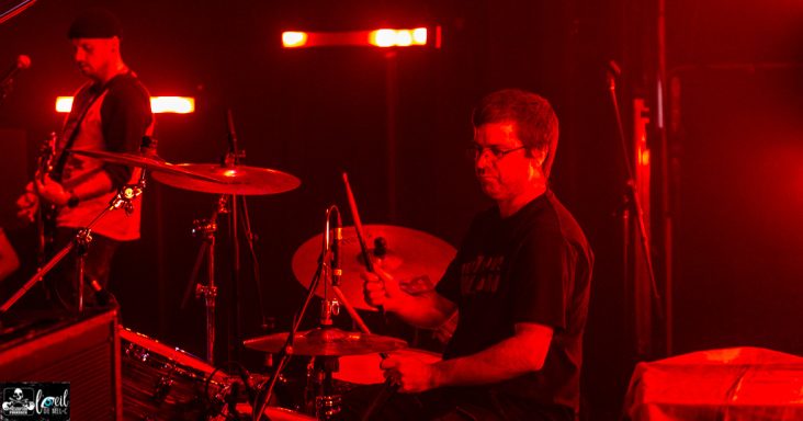 Musicians performing on stage, with a drummer highlighted in red lighting.