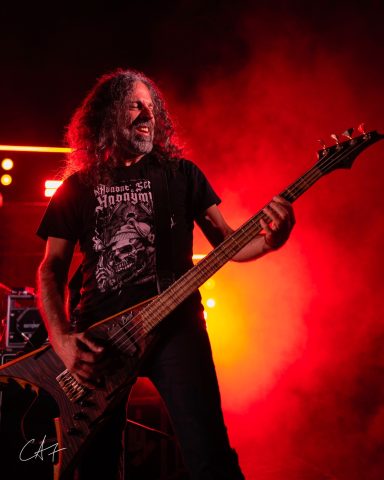 Musician playing bass guitar on stage with dramatic red lighting.