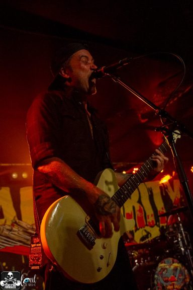 Musician performing live on stage, playing an electric guitar with vibrant lighting.