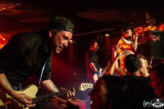 A guitarist performs passionately on stage while fans enjoy the energetic atmosphere.