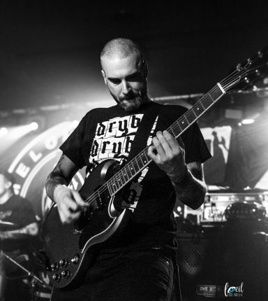 Man playing guitar on stage, wearing a black t-shirt with graphic design.