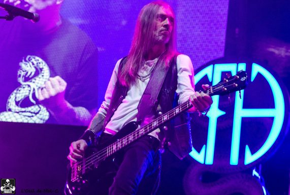 A musician playing bass guitar on stage, with vibrant lighting in the background.