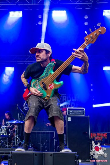Musician playing a bright blue bass guitar on stage with vibrant lighting.