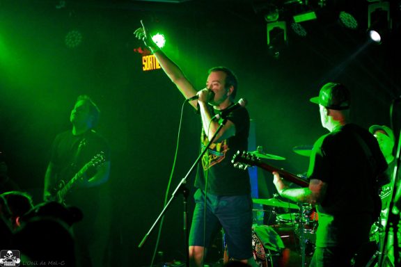 Band performing on stage with green lighting, lead singer gesturing passionately.