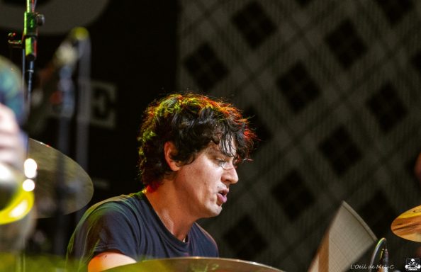 Drummer playing passionately on stage, with focused expression and dynamic lighting.