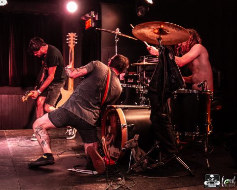 Band performing on stage with guitar, drums, and energetic motion.
