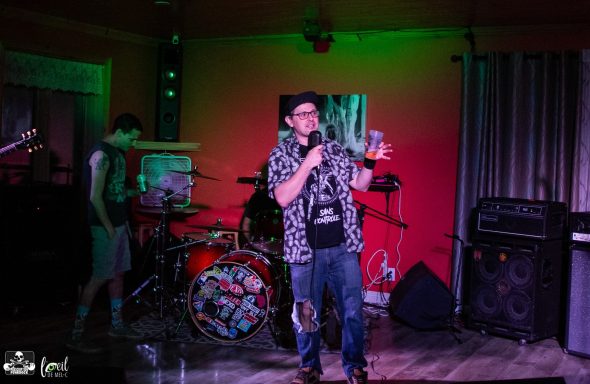 Person speaking on stage in front of musical instruments and dim lighting.