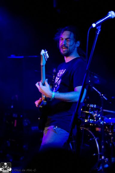 A musician playing guitar on stage with a vibrant blue light backdrop.