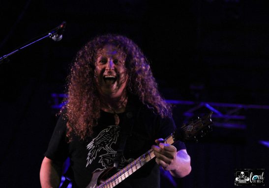 Smiling musician with curly hair playing guitar on stage.