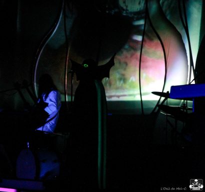 A dark performance scene with silhouettes and colorful projections in the background.