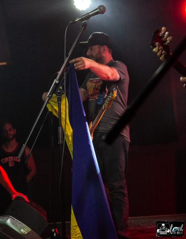 A performer holds a yellow and blue flag on stage during a concert.