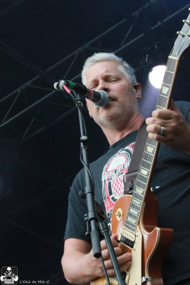 Musician singing into a microphone while playing an electric guitar on stage.