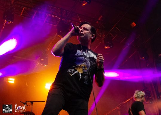 A vocalist performs on stage with colorful lights in the background.