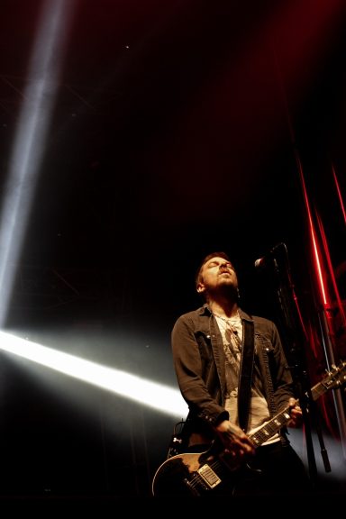 Performer on stage with guitar, illuminated by dramatic lighting.
