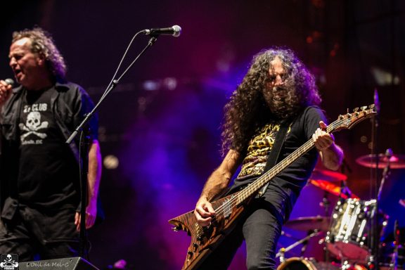 Musicians performing on stage, one singing and the other playing electric guitar.