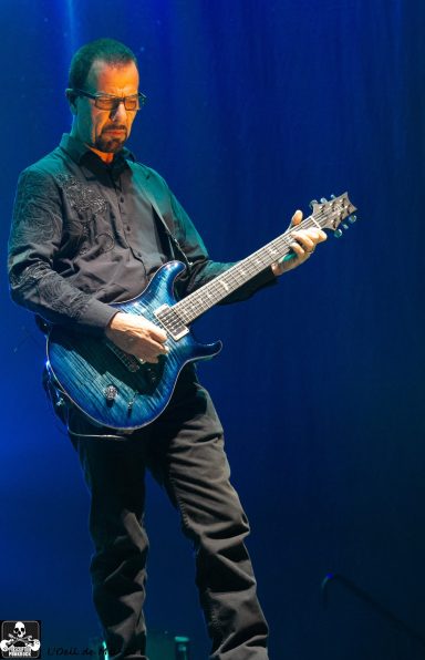Person playing a blue electric guitar on stage with dramatic blue lighting.