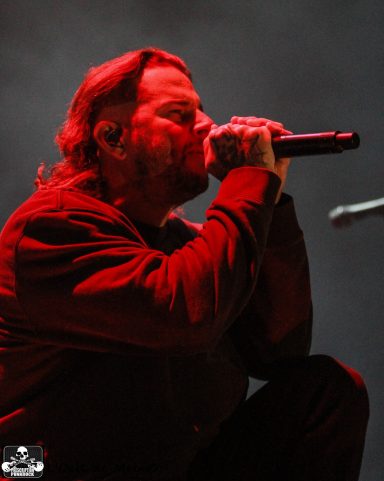 A singer in a black outfit performing on stage, illuminated by red lighting.
