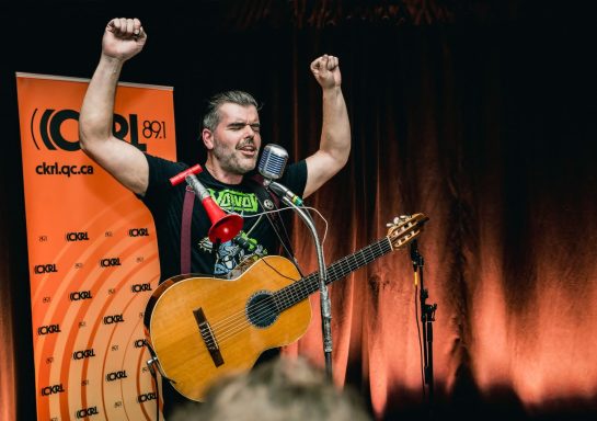 Pépé et sa guitare - Radiothon CKRL 89,1 Musician performing energetically with a guitar and raising hands on stage.