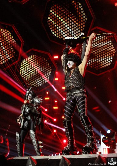 Two musicians perform on stage; one raises a guitar, while the other stands nearby.