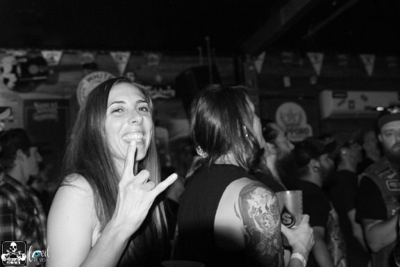 A woman smiles and gestures with a hand sign in a crowded venue.