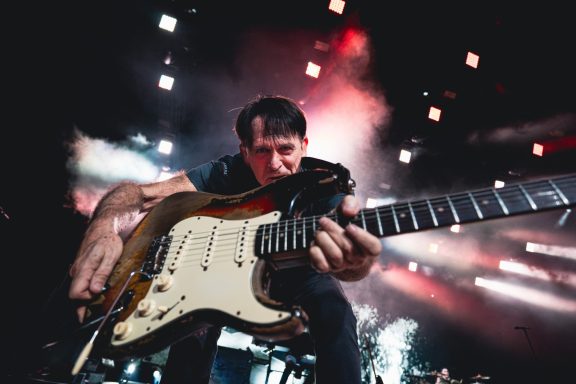 A guitarist performs passionately on stage with colorful lights in the background.