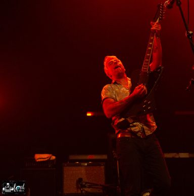 guitarist passionately performing on stage with red lighting.
