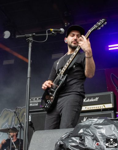 A musician playing electric guitar on stage, with amplifiers in the background.